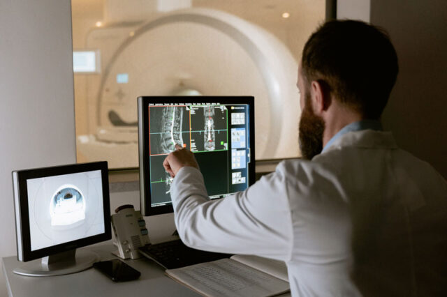 Imagen de un médico observando una pantalla mientras revisa una tomografía computarizada (TC) de un paciente